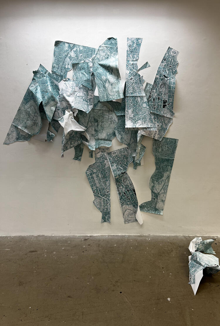 An abstract shape made of strips of old Edinburgh map looms taller than a human from a stark white wall. A crumpled piece of map sits on a grubby concrete floor. The arrangement of the piece is meant to evoke Jacob facing the Angel in the story from the To